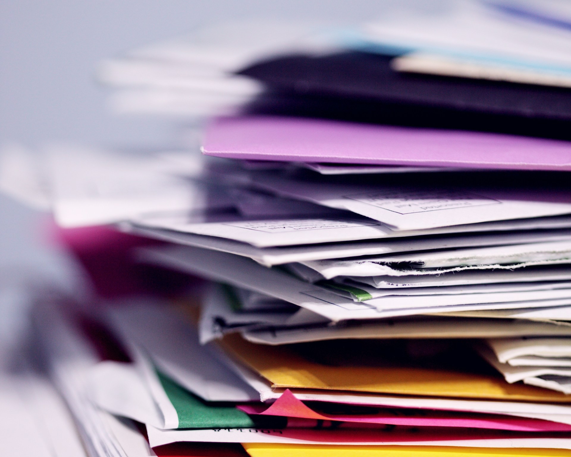 A tall, disorganised stack of mixed paper business documents and coloured folders in close-up, representing the manual document handling that cbs AID and SAP Business AI convert into SAP-ready data.